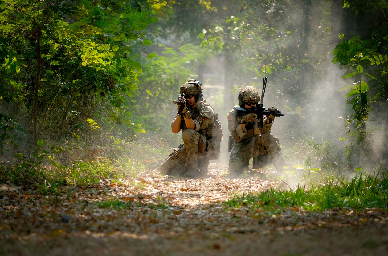 Two soliders crouch in a forest aiming their weapons
