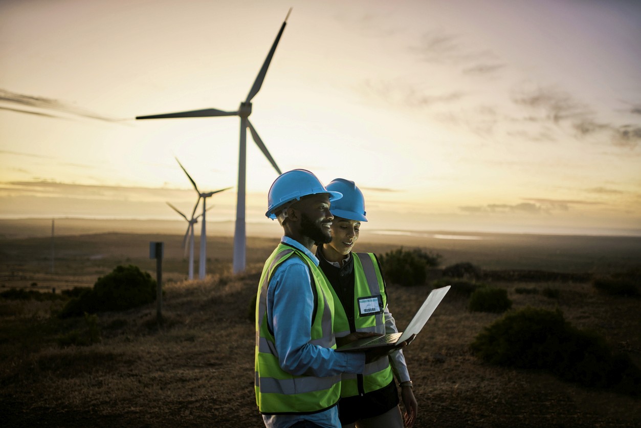 Two inspectors look over the hills with wind turbines in the background