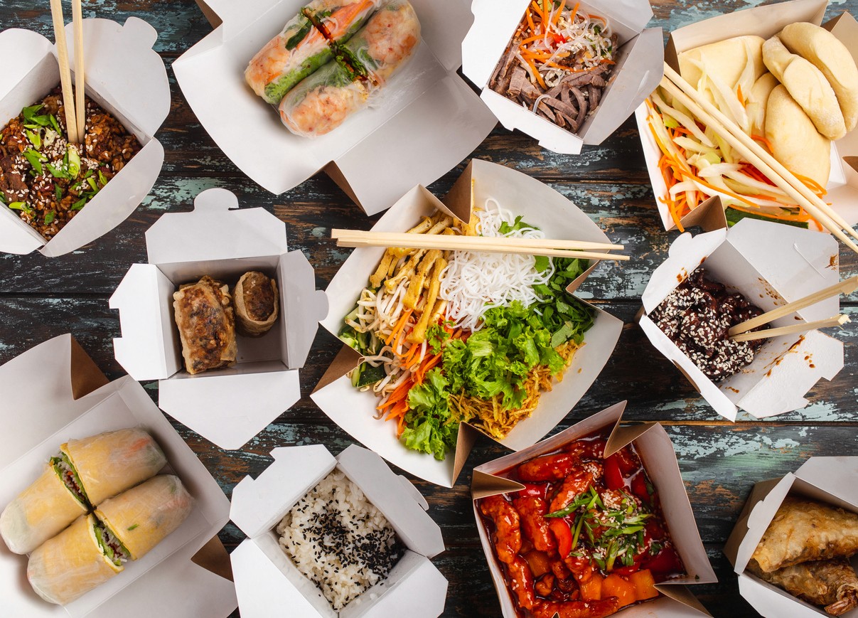 Multiple boxes of take out food spread across a table