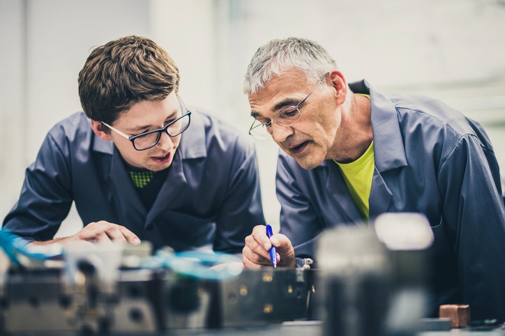 Two technicians closely examine a small machine