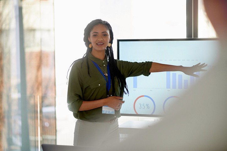 A woman conducting a presentation with a slide of graphed data