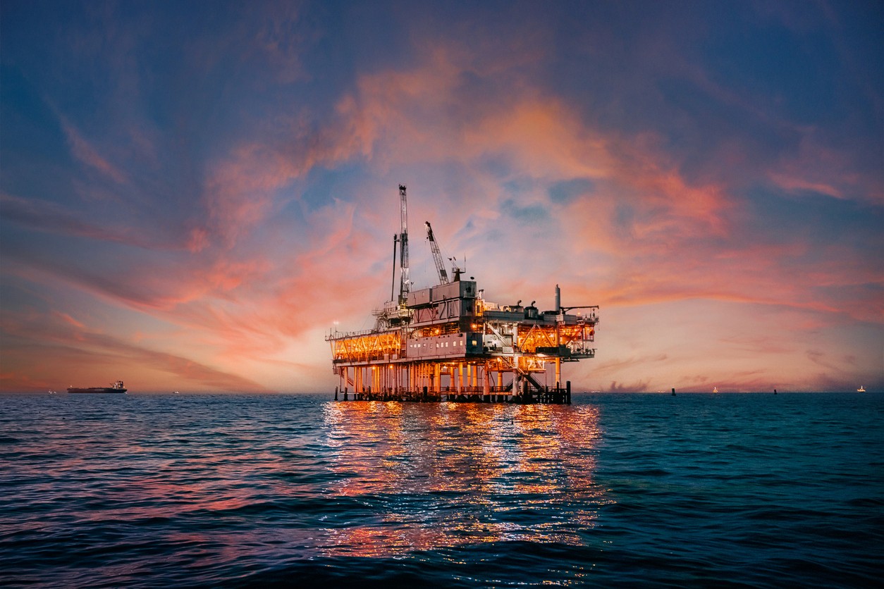 An oil rig facility in the middle of the ocean with the sun setting in the background